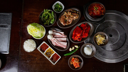 Top view Korean Grilled BBQ combo with pork belly and marinated pork set on the traditional grill table, with lettuce, dipping sauce and pickle dishes