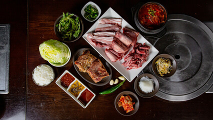 Top view of Korean Grilled BBQ combo with pork belly, wagyu, marinated beef set on the traditional grill table, with lettuce, dipping sauce and pickle dishes