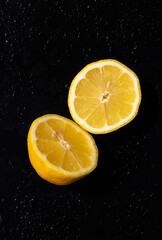 Ripe yellow lemon fruit cut in half isolated on black background in water drops.
