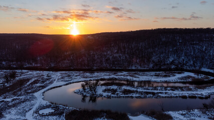 Winter aerial panorama view on snowy river curve with scenic reflection. Zmiyevsky region on Siverskyi Donets River in Ukraine. Sunset sun shining above woody hill