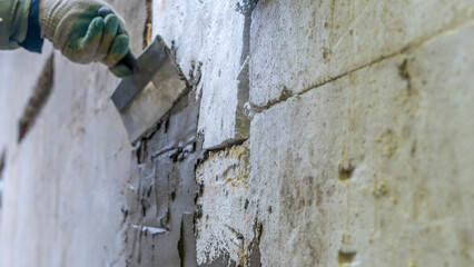 A plasterer applies plaster with a spatula to a brick wall. Wall renovation process. Defocused background.