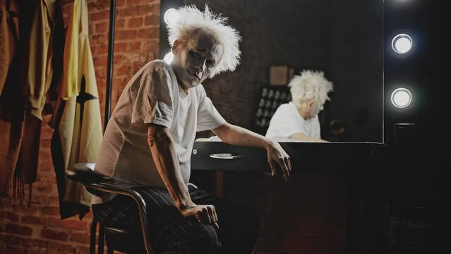 Depressed mime with tousled hair sits in dressing room