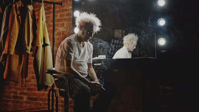 Mime smokes cigarette against mirror in dressing room