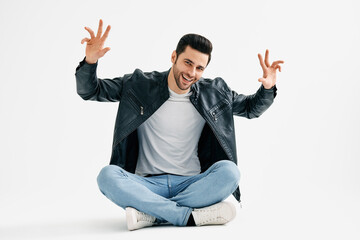 Positive smiling young man wave hands sitting with legs crossed on floor isolated over white...