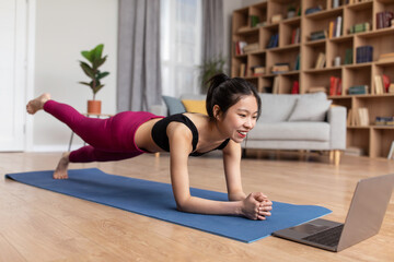 Fototapeta na wymiar Fit asian woman standing in elbow plank, lifting her leg, exercising at home and following online video tutorial
