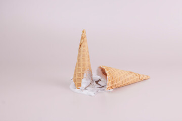 Melting ice cream with broken empty waffle cones on pastel color backgrounds. Summer creative food concept.