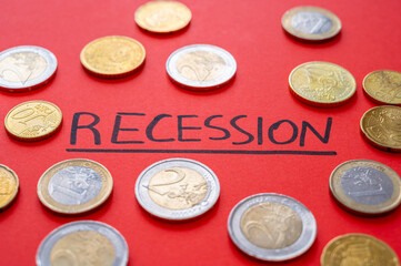 Text "recession" written on red surface and few coins around. Poverty and economic difficulties due to recession and economic crisis.
