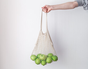 White string bag with green apples on a white background.