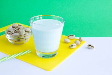 Pistachio milk in the drinking glass on the colored background. Closeup.
