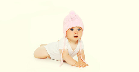 Portrait close up of cute baby crawling on the floor wearing pink winter knitted hat on white background