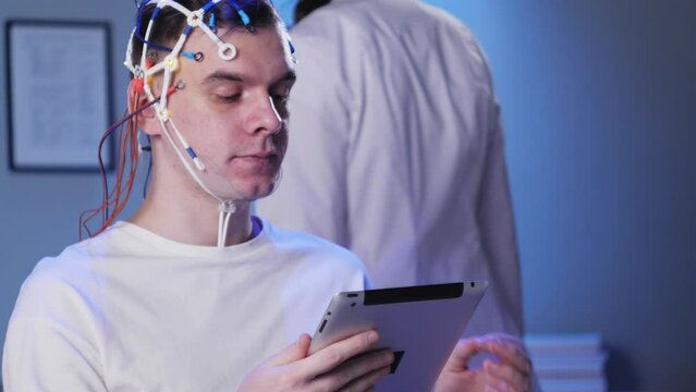 Man wearing EEG topographer for examining brain, doctor making electrogram of scalp activity. Researching of brain work using electroencephalography headset.