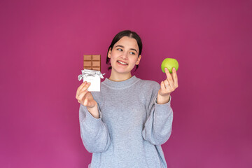 A young woman with an apple and a chocolate bar on a pink background.