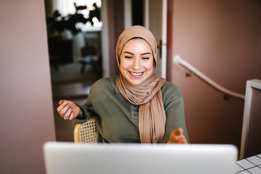 Smiling female freelancer in hijab doing video call through laptop at home