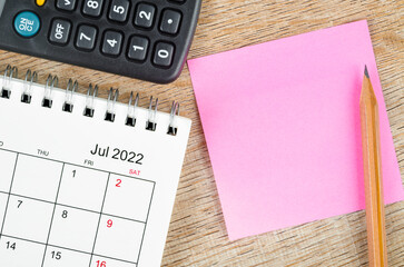 Blank sticky note on July 2022 desk calendar on wooden background for your text.