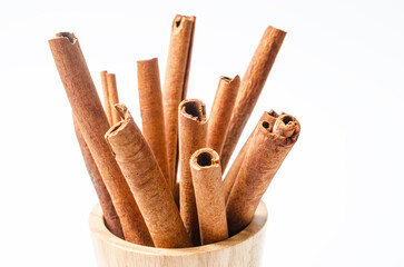 Group of cinnamon sticks in wooden cup on white background.