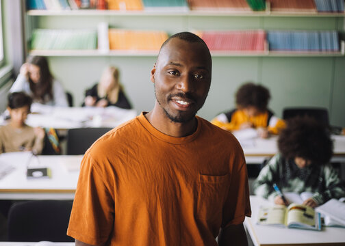 Portrait Of Smiling Male Teacher With Students Studying In Classroom