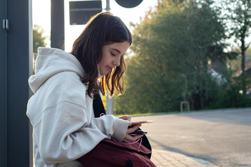 A young teenage woman is waiting for a bus at a bus stop early in the morning.