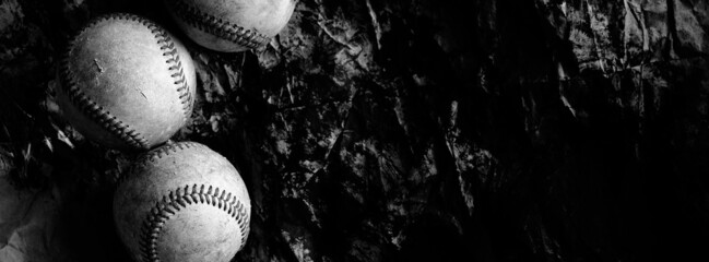 Group of old vintage baseball balls on dark grunge background banner in black and white.