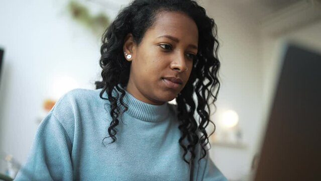 Meditative African woman wearing blue sweater typing by laptop in cafe