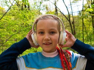 Adorable child girl in headphones learning language listening to music podcast with smartphone...