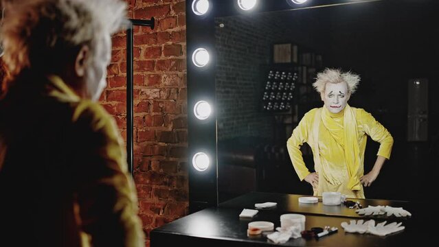 Angry mime looks at reflection in mirror in dressing room