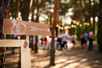 Wooden arrow sign with wedding rings on ceremony venue. Wedding party banner post . Direction info...