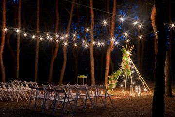 Festive string lights illumination on boho tipi arch decor on outdoor wedding ceremony venue in...