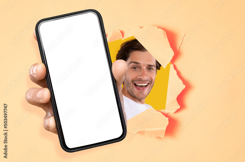 Poster cheerful guy showing white empty smartphone screen through torn paper