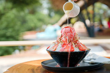 Japanese shaved ice dessert , Hand pouring sweet condensed milk on ice cream. Served with strawberry kakigori bingsu topped with almond stick strawberry sauce. Traditional summer dessert in Japan.