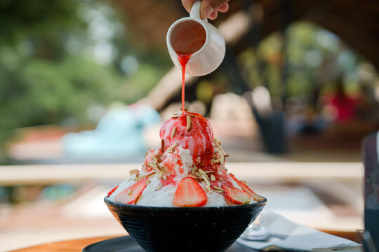 Japanese Shaved Ice Dessert , Hand Pouring Sweet Strawberry Sauce On Ice Cream. Served With Strawberry Kakigori Bingsu Topped With Almond Stick Condensed Milk. Traditional Summer Dessert In Japan.