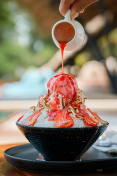 Japanese shaved ice dessert , Hand pouring sweet strawberry sauce on ice cream. Served with strawberry kakigori bingsu topped with almond stick condensed milk. Traditional summer dessert in Japan.