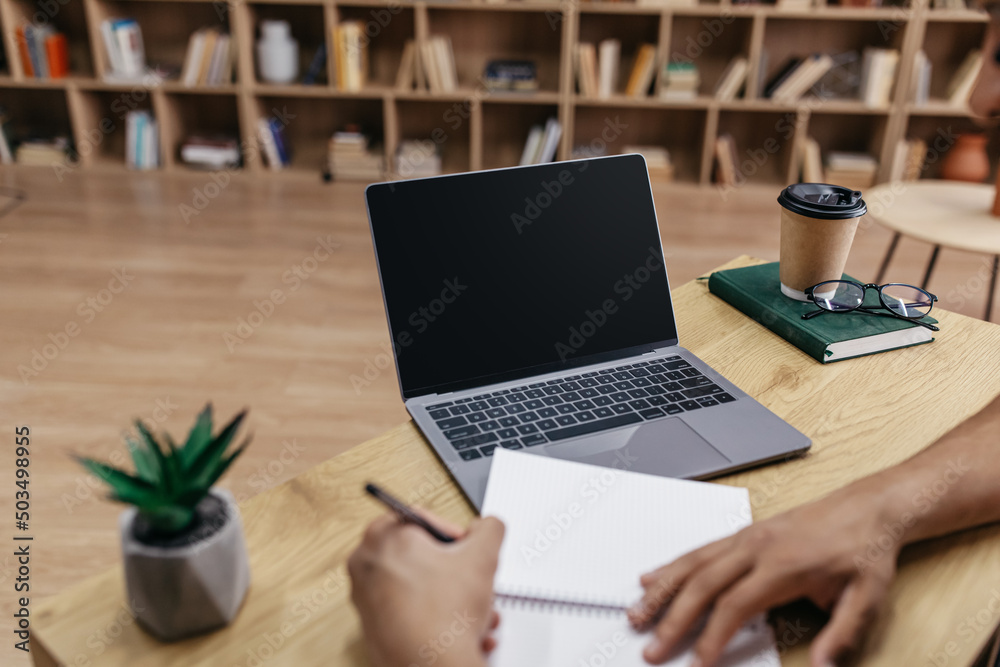 Poster Online class concept. Male student writing in notebook, taking notes and using laptop with black screen for mockup