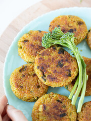 Crispy fried meatless quinoa fritters (savory patties or pancakes) served with fresh broccoli on a plate isolated on a wooden table. Top view from above. Healthy meat-free plant-based cooking concept.