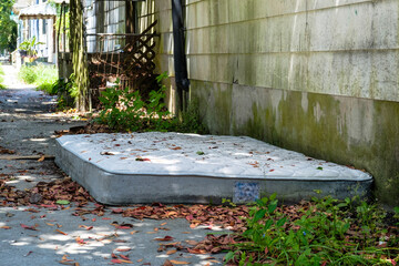 Discarded moldy mattress on the ground between an old beat up house and a sidewalk in New Orleans,...