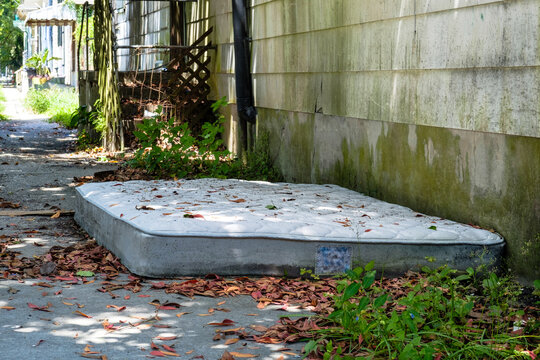 Discarded Moldy Mattress On The Ground Between An Old Beat Up House And A Sidewalk In New Orleans, LA, USA