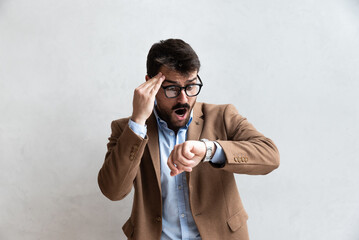 Young business man in suit with eyeglasses with shocked facial expression looking at wristwatch because he is late. Time management concept 