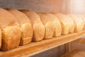 Close-up of freshly baked bread on wooden shelves, photo with illumination. Production of bakery products