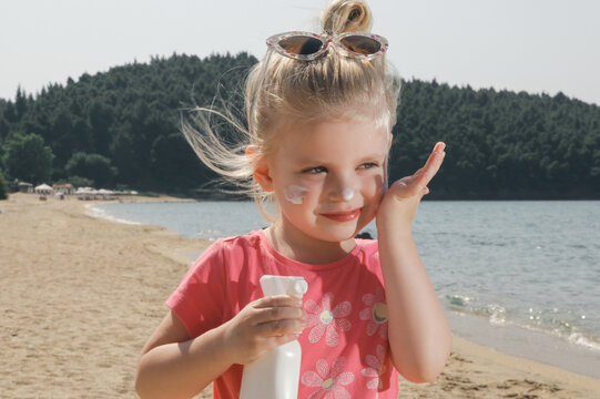 Cute Little Toddler Girl Applying Sunscreen Protection Cream On The Beach. Sun Blocking Lotion For Protecting Baby From Sun During Summer Vacation. Children Skin Care During Travel Time.