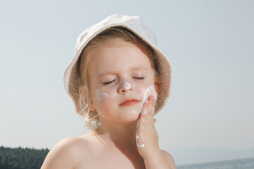 Cute little toddler girl applying sunscreen protection cream on the beach. Sun blocking lotion for...
