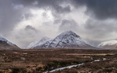 Beautiful Winter landscape image of Stob Dearg Buachaille Etive Mor viewed from Rannoch Moor with snowcapped peak and beautiful moody cloud formations