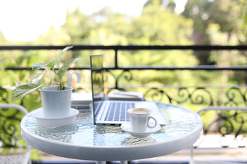Laptop front view and coffee cup with notebooks on white glass table outdoor