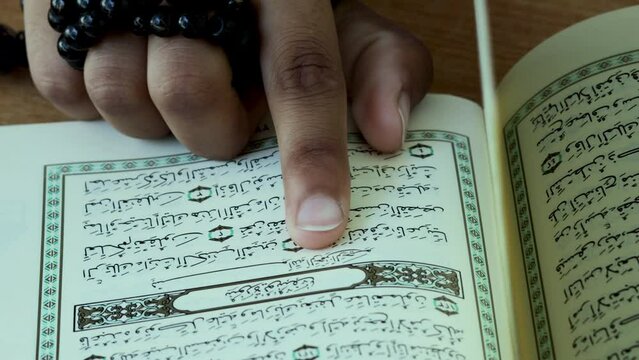 The index finger of a Woman spells one by one the Arabic letters in the Quran at Surah Yusuf, 12th chapter of the Qur'an.  India, Pakistan, Indonesia - May 08, 2022.