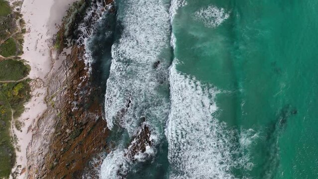 Turquoise ocean waves wash up on empty rugged Cape Town beach - aerial top down