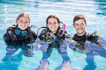 A group of happy scuba divers standing in a pool with their gear on smiling at the camera