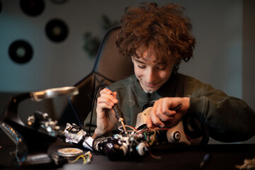 A smart young teenager learns electronics and soldering wire leads in robotics. A child works on a...