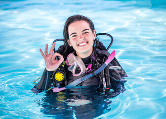 Young woman with scuba gear on in a pool smiling at the camera showing the OK sign