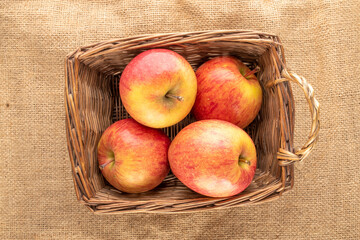 Several red organic apples in a basket on jute fabric, close-up, top view.
