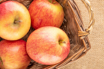 Several red organic apples in a basket on jute fabric, close-up, top view.