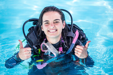 Young woman with scuba gear on in a pool smiling at the camera showing thumbs up