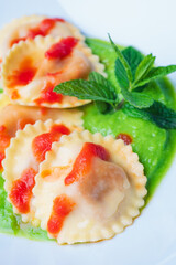 closeup of Italian pasta ravioli with burrata filling with tomato and pea cream on white plate shot from above in vertical shot